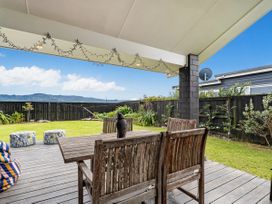 An outdoor patio with a wooden table and chairs on a deck overlooking a grassy yard with plants and a black fence at Tide and Tranquility Whitianga