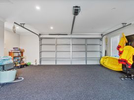 A garage with closed double metal doors and various storage items including a bookshelf and life jackets at Tide and Tranquility - Whitianga Holiday Home in Whitianga