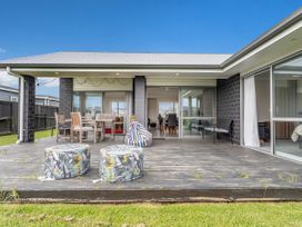 An outdoor wooden deck with two patterned cushions and a bean bag in front of a house with sliding glass doors at Tide and Tranquility - Whitianga Holiday Home in Whitianga