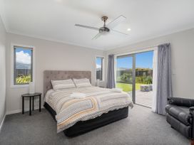 A bedroom with a bed two windows a sliding glass door a black side table a black armchair and a ceiling fan at Tide and Tranquility - Whitianga Holiday Home in Whitianga
