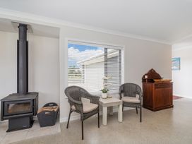 A seating area with two wicker chairs and a small table next to a wood stove and a wooden cabinet at Tide and Tranquility Whitianga