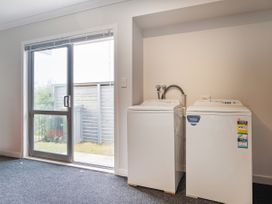 A laundry area with a washing machine and dryer next to a glass sliding door at Tide and Tranquility - Whitianga Holiday Home Whitianga