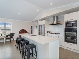 A kitchen with a long island and four black stools in Tide and Tranquility Whitianga Holiday Home Whitianga