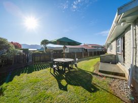 A backyard with a round table and chairs under an umbrella next to a house at Cosy Crib - Te Anau Holiday Home in Te Anau