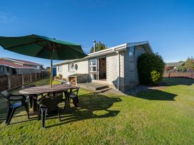 A backyard with a round wooden table and black chairs under a green umbrella at Cosy Crib - Te Anau Holiday Home Te Anau