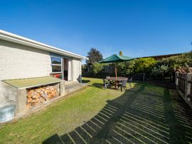 A backyard with a woodpile next to a house and a round table with chairs and a green umbrella in Te Anau