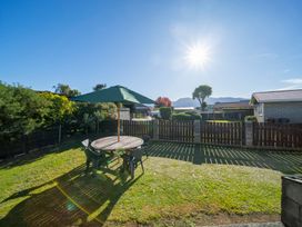 A backyard with a round table and chairs under a green umbrella beside a fence and bushes at Cosy Crib - Te Anau Holiday Home in Te Anau