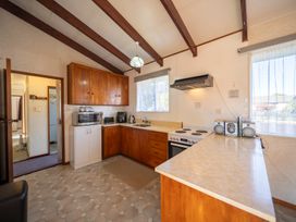 A kitchen with wooden cabinets stove microwave and windows at Cosy Crib - Te Anau Holiday Home in Te Anau
