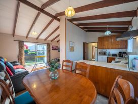 A dining table with chairs and a vase of flowers next to a kitchen and living area with a sofa and sliding door at Cosy Crib - Te Anau Holiday Home in Te Anau