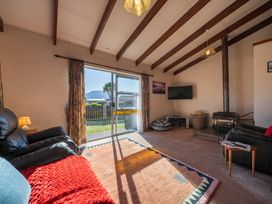 A living room with a sliding glass door leading outside two black leather couches a wood stove and a wall-mounted television at Cosy Crib - Te Anau Holiday Home in Te Anau