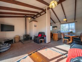 A living room with a wood stove next to a black armchair and a dining table with chairs near a window at Cosy Crib - Te Anau Holiday Home in Te Anau