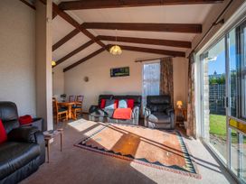 A living room with black leather sofas, a wooden dining table with chairs, a large carpet, and sliding glass doors at Cosy Crib - Te Anau Holiday Home in Te Anau