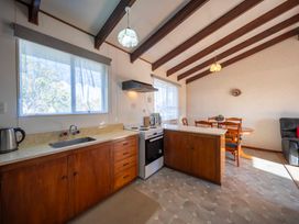 A kitchen and dining area with wooden cabinets a stove a round dining table and chairs at Cosy Crib - Te Anau Holiday Home in Te Anau