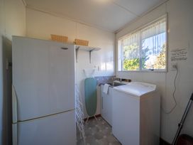 A laundry room with a white refrigerator ironing board washing machine and a window at Cosy Crib - Te Anau Holiday Home in Te Anau