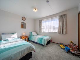 A bedroom with two single beds a wooden nightstand toys on the floor and a window with curtains at Cosy Crib - Te Anau Holiday Home in Te Anau