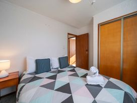 A bedroom with a double bed with geometric patterned bedding two blue pillows a wooden nightstand with a lamp and built in wooden wardrobe at Cosy Crib - Te Anau Holiday Home in Te Anau