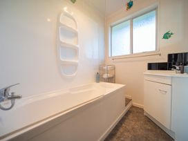 A bathroom with a bathtub a sink a window and a towel rack at Cosy Crib - Te Anau Holiday Home in Te Anau