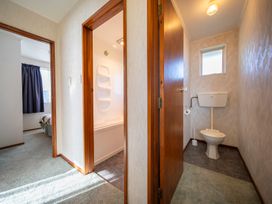 A hallway with doorways leading to a bedroom with a bed and curtain a bathroom with a bathtub and a separate toilet room at Cosy Crib - Te Anau Holiday Home in Te Anau