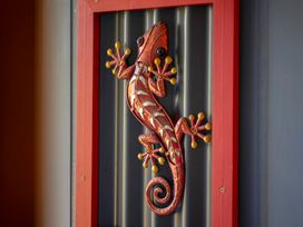 A metal gecko wall decoration mounted on a corrugated metal surface with a red frame at Cosy Crib - Te Anau Holiday Home in Te Anau