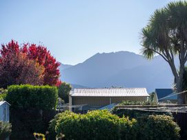 A backyard with bushes and trees near a metal shed with mountains in the background at Cosy Crib - Te Anau Holiday Home Te Anau