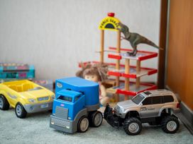 Toy cars a toy dinosaur a doll and a toy parking garage on a carpeted floor at Cosy Crib - Te Anau Holiday Home in Te Anau