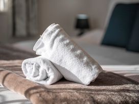 Two rolled white towels on a brown blanket on a bed at Cosy Crib - Te Anau Holiday Home in Te Anau