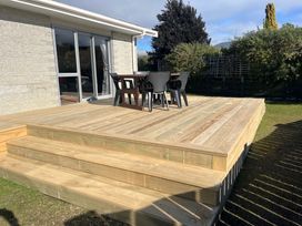 An outdoor area with a wooden deck, table, and chairs at Cosy Crib - Te Anau Holiday Home, Te Anau