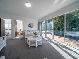 A living room with a white sofa a white coffee table and sliding glass doors opening to a deck at Relaxing Kiwi Bach - Te Anau Holiday Home in Te Anau