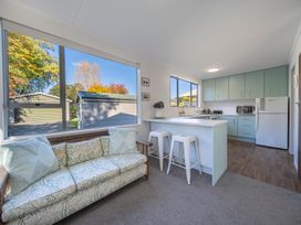 A living room with a patterned sofa and a kitchen with light blue cabinets and white stools at Relaxing Kiwi Bach Te Anau Holiday Home in Te Anau