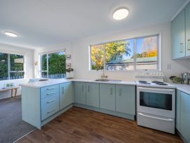 A kitchen with blue cabinets white countertops a white stove a sink and large windows showing trees outside at Relaxing Kiwi Bach in Te Anau
