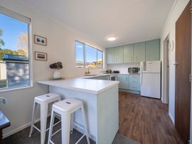 A kitchen with light blue cabinets white countertop two white stools and a refrigerator at Relaxing Kiwi Bach Te Anau Holiday Home in Te Anau