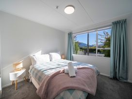 A bedroom with a bed covered in checkered bedding and a pink blanket next to a window with blue curtains and two bedside tables with lamps at Relaxing Kiwi Bach Te Anau Holiday Home in Te Anau