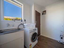 A laundry room with a washing machine a sink a laundry basket and a vacuum cleaner at Relaxing Kiwi Bach Te Anau Holiday Home in Te Anau