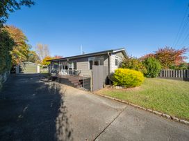 A single-story house with a driveway leading to a garage and a front yard with bushes and trees at Relaxing Kiwi Bach Te Anau Holiday Home in Te Anau