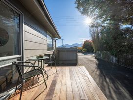 A wooden deck with two black chairs and a glass table with a small plant by a house exterior at Relaxing Kiwi Bach Te Anau Holiday Home in Te Anau