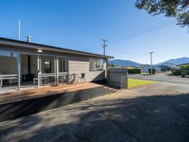 An outdoor deck with two chairs and a table outside a house with sliding glass doors in a residential neighborhood at Relaxing Kiwi Bach Te Anau