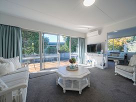 A living room with white furniture including sofas and a coffee table a flat screen tv and sliding glass doors leading to an outdoor deck at Relaxing Kiwi Bach - Te Anau Holiday Home in Te Anau