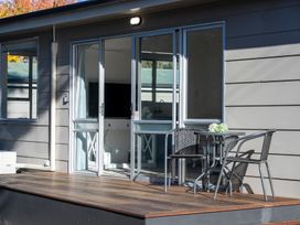 A small outdoor wooden deck with a round table and two chairs outside sliding glass doors at Relaxing Kiwi Bach Te Anau Holiday Home in Te Anau