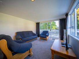 A living room with blue upholstered wooden sofa and armchairs a wooden table with a TV and large sliding glass doors at Relaxing Kiwi Bach - Te Anau Holiday Home in Te Anau