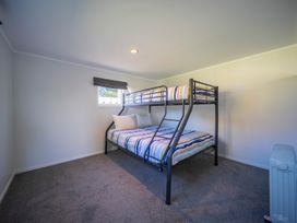 A bedroom with a bunk bed with striped bedding and a window at Relaxing Kiwi Bach - Te Anau Holiday Home in Te Anau