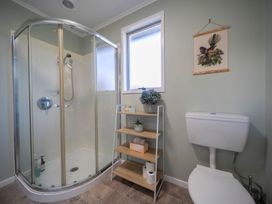 A bathroom with a corner shower, a toilet, a wooden shelf with plants and toiletries, and a bird picture on the wall at Relaxing Kiwi Bach Te Anau Holiday Home in Te Anau
