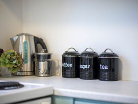 A kitchen countertop with a kettle a French press a glass and three black canisters labeled coffee sugar and tea at Relaxing Kiwi Bach - Te Anau Holiday Home in Te Anau
