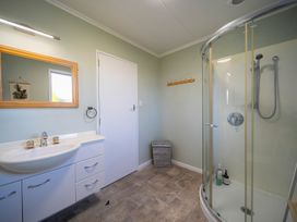 A bathroom with a sink and mirror a shower enclosure a door and a laundry basket at Relaxing Kiwi Bach Te Anau