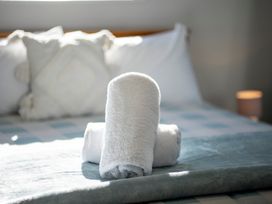 Two rolled white towels on a bed with pillows and a lamp in the background at Relaxing Kiwi Bach in Te Anau