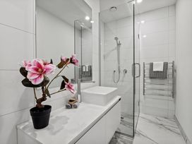 A bathroom with a sink countertop with a flower pot and towels a glass shower enclosure and a towel rack at Remarkable QT  - Queenstown Holiday Home in Queenstown