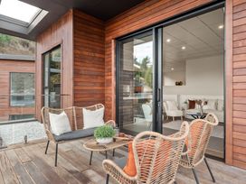 An outdoor deck with wicker furniture and cushions next to a sliding glass door leading to a living room at Remarkable QT  - Queenstown Holiday Home in Queenstown