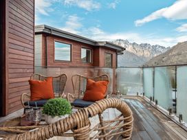 A balcony with wicker chairs and orange cushions overlooking mountains at Remarkable QT  Queenstown