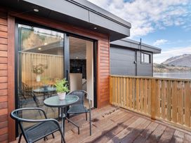 A balcony with a small round glass table and two chairs overlooking a lake and mountains at Remarkable QT  Queenstown