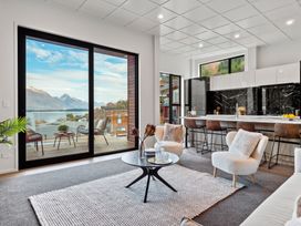 A living room with armchairs and a round table next to a kitchen with bar stools and a balcony overlooking mountains at Remarkable QT  Queenstown Holiday Home