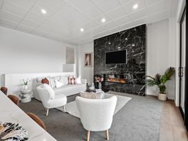 A living room with white chairs a gray sofa and a black marble fireplace with a mounted TV at Remarkable QT  Queenstown Holiday Home in Queenstown